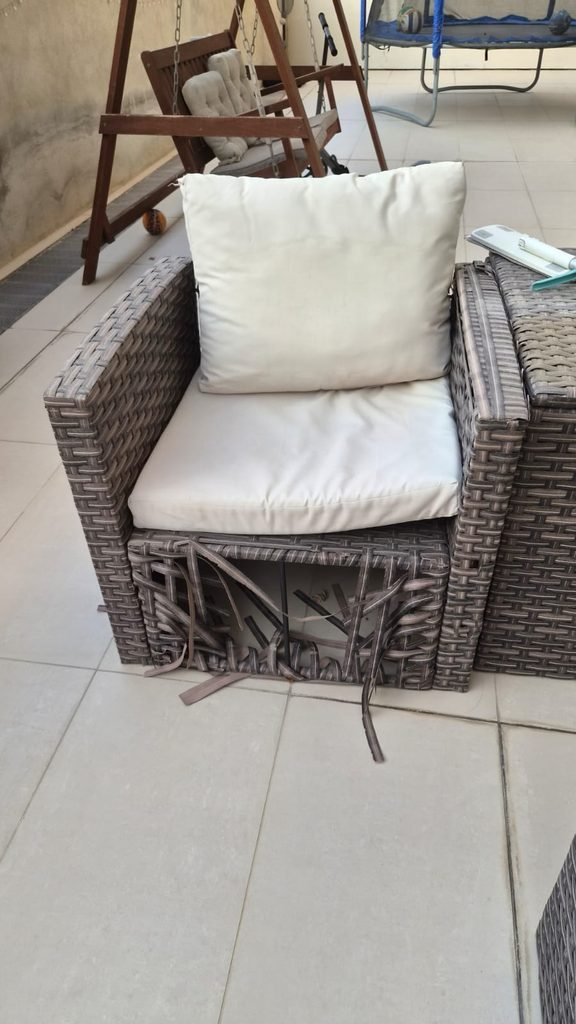 An outdoor wicker armchair with white seat and back cushions and damaged weaving near the base. The image can support content about old furniture pickup and removal services.