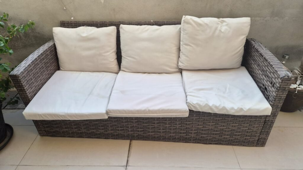 Brown wicker two-seater outdoor sofa with white cushions for furniture removal in Abu Dhabi
